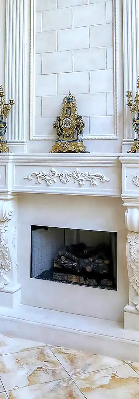 Elegant cast stone fireplace mantel with intricate detailing, flanked by built-in shelves displaying decorative items.