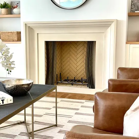 Elegant limestone fireplace surround set in a cozy living space with leather seating and modern decor elements.