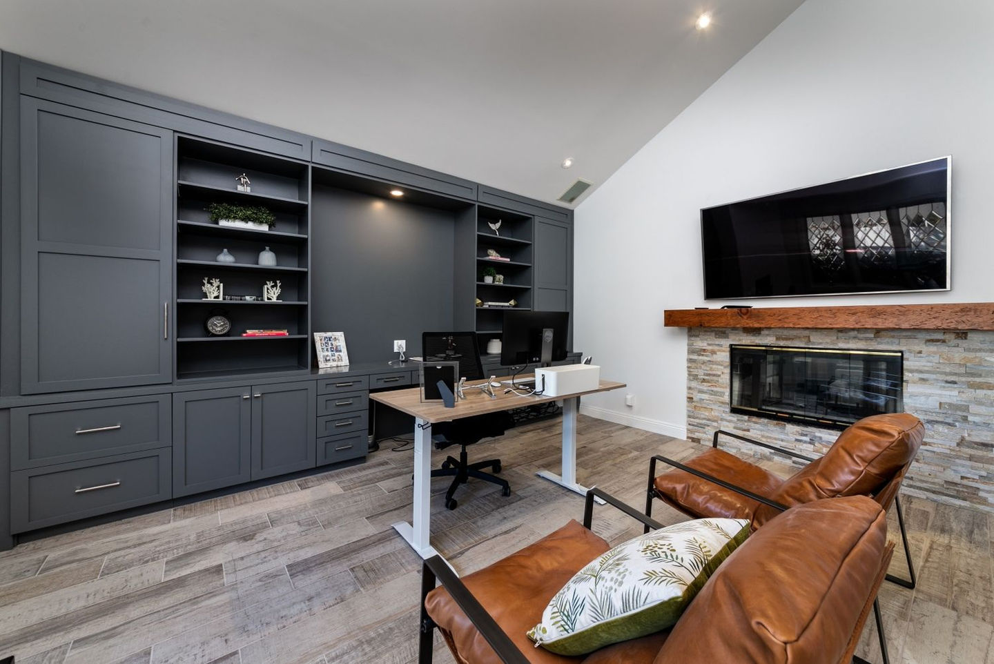 Modern office with leather chairs, a wooden desk, and a fireplace under a wall-mounted TV.