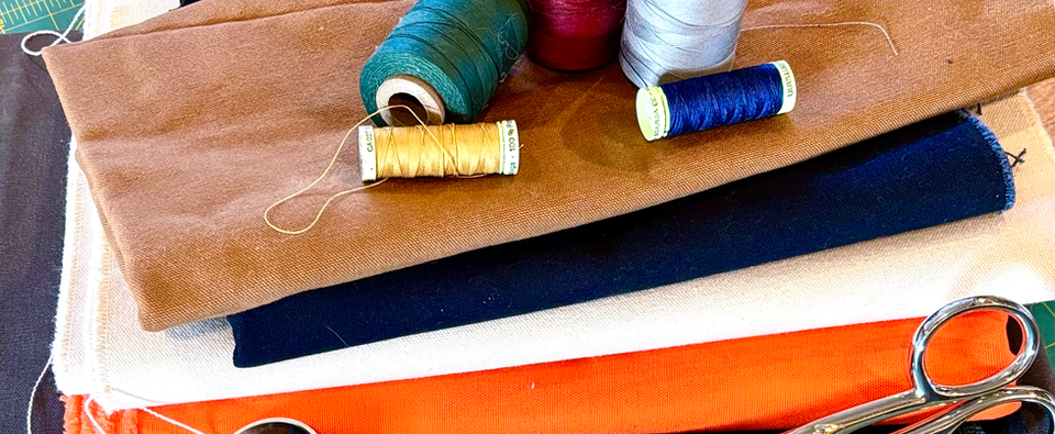 Fabric of several solid colors stacked with scissors and thread as accents.