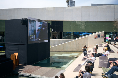 people sitting near water watching outdoor screen at OFFF Barcelona, creative space focused on 3D, CGI, cinema 4d and visual storytelling