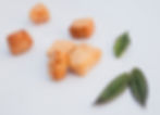 Brown cheese puffs scattered on a white surface, accompanied by two green leaves. Bright and minimalistic setting.