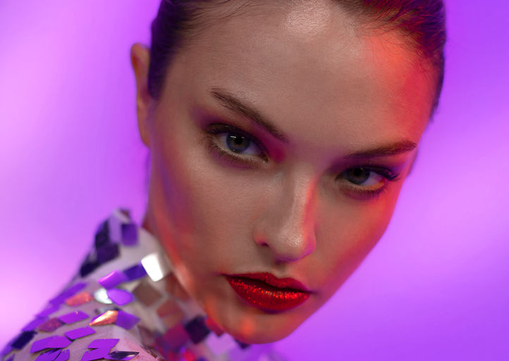 Close-up editorial portrait of India Gants in mirror sequin top with red lips against purple background, photography by Tatiana Sitnik