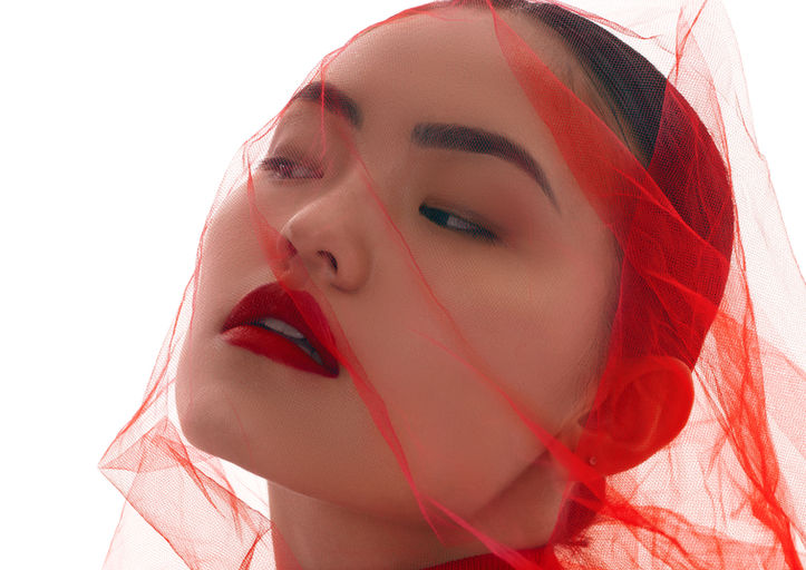 Dramatic editorial portrait of woman in red dress draped in red tulle veil against white background, photography by Tatiana Sitnik