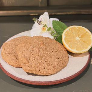 A photograph of two cookies on a plate with a garnish of rose, Tulsi and a half of a lemon