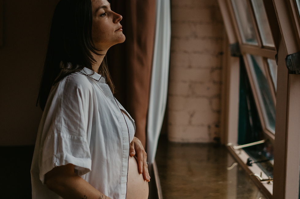 Schwangere Frau steht am Fenster und hält sich den Bauch
