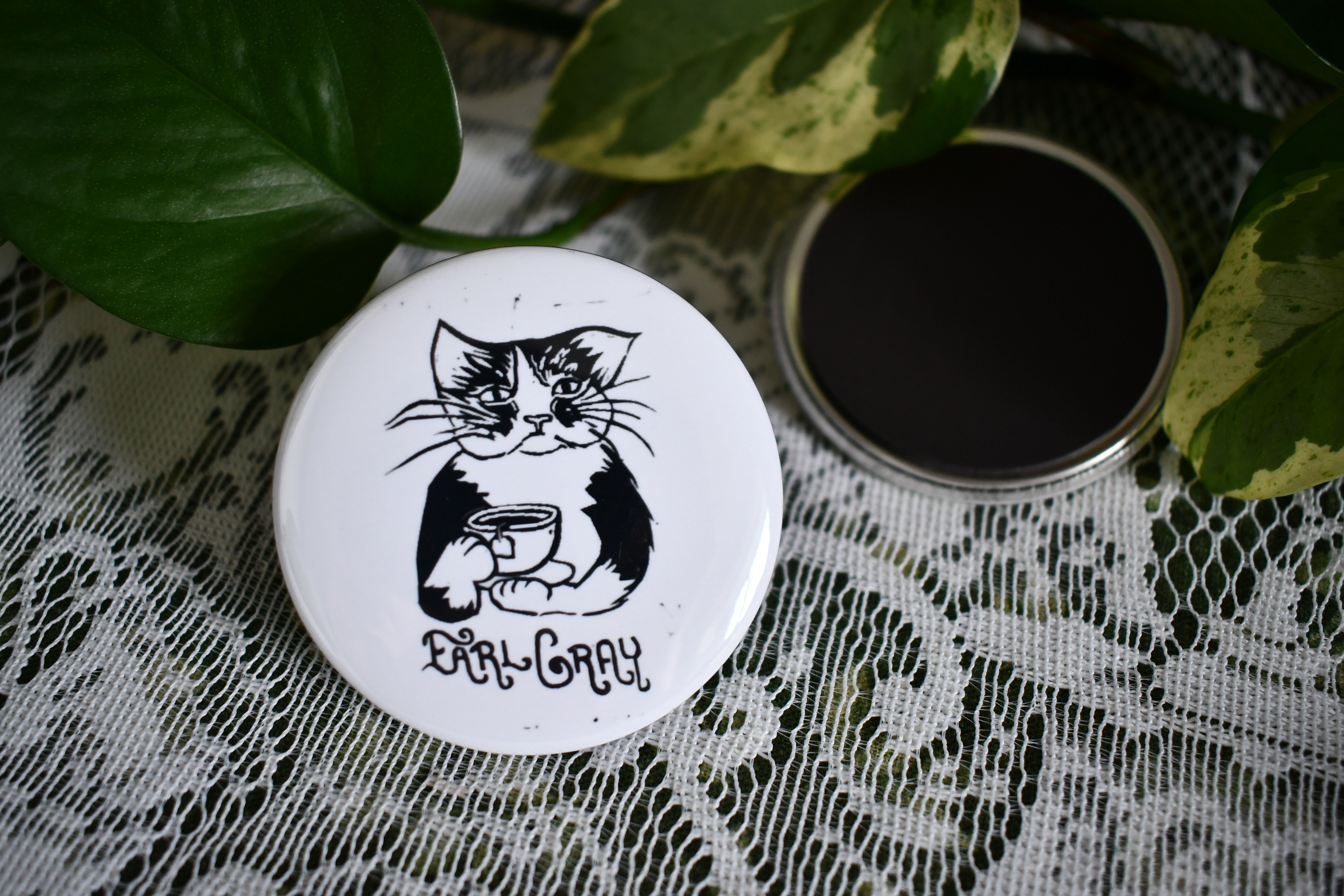 White button magnet with cat illustration holding cup of Earl Gray tea.