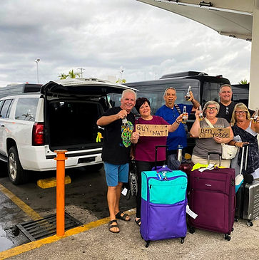 Happy group of travelers with welcome signs next to white Chevy Suburban SUV for private airport transfer from Puerto Vallarta Airport by Riviera Go Transport