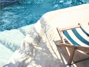 Sunny day with palm tree shadow on floor with striped chair and pool.