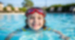 girl swimming in pool with goggles and smiling
