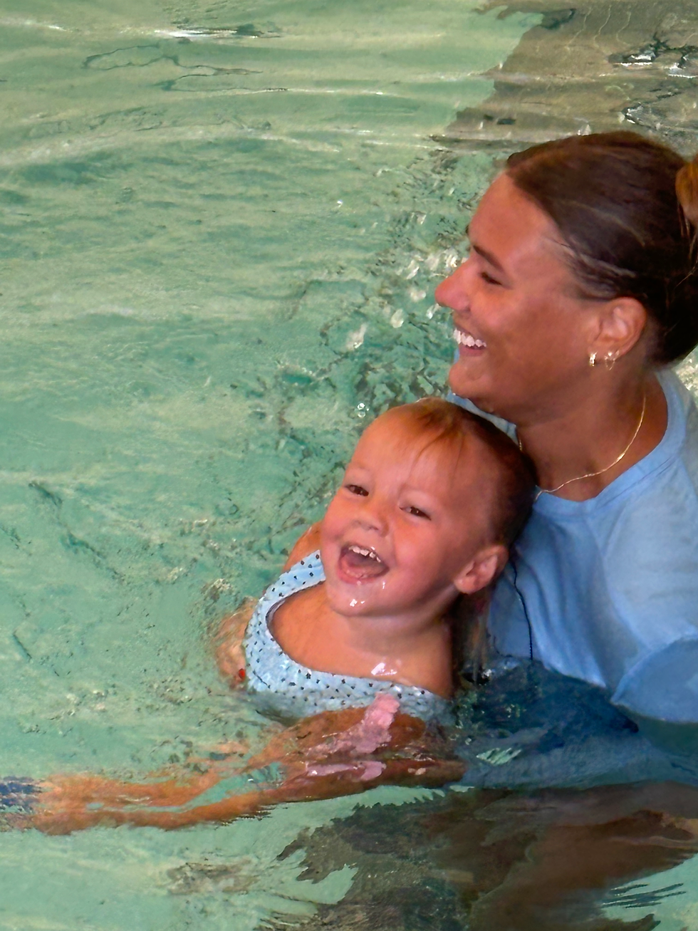 swim instructor smiling in pool holding toddler swimmer