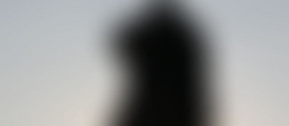 Silhouette of a woman standing alone against an open sky, gazing toward the horizon.