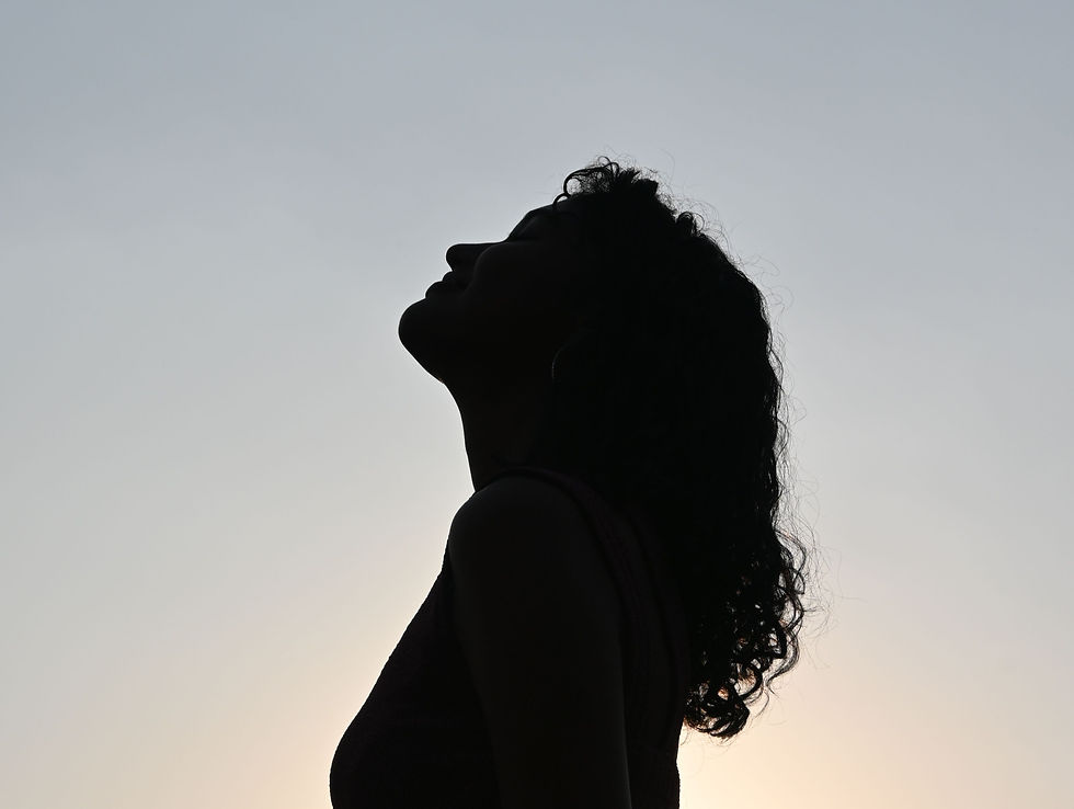 Silhouette of a woman standing alone against an open sky, gazing toward the horizon.