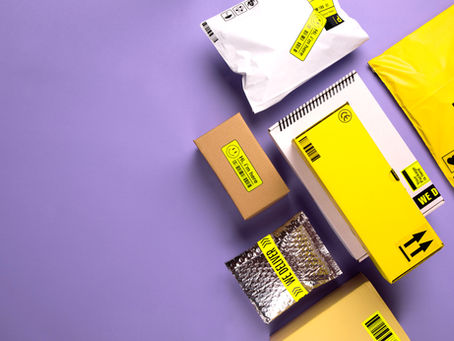 Shipping packages on purple background, featuring yellow, silver, and brown boxes. Text: "WE DELIVER" and "Handle with care."