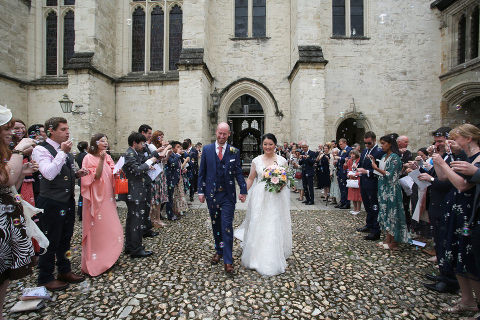A bride and groom walking out of church. Their wedding guests are blowing bubbles. 