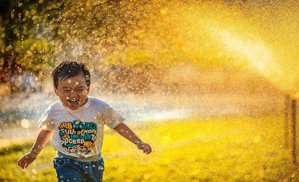Photo of a young boy smiling and running through a sprinkler.