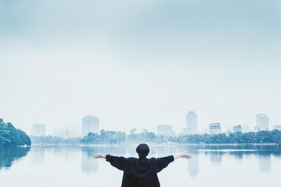 Photo of a young woman with open arms facing a lake.