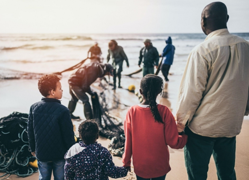 Photo of a refugee family holding hands on the beach of their country of refuge.