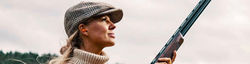 Beautifully blonde lady standing poised, ready with over & under shotgun, wearing shooting cap.
