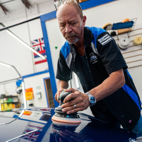 Master detailer performing a final polish and inspection on a vehicle's hood under professional studio lighting.