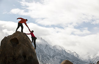 A man is helping another person to reach the top of a mountain