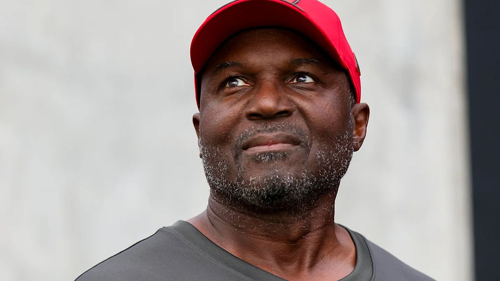 Close-up of a man in a red cap and gray shirt looking upward with a thoughtful expression against a plain background
