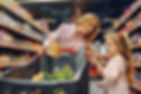 A mom and daughter at supermarket pushing the cart and looking at shopping list.