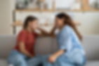 Mom and daughter sitting on couch smiling at each other.