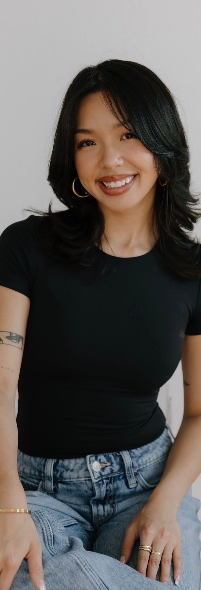 Portrait photo of a woman sitting, smiling at the camera, neutral background, vertical portrait