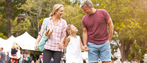 A family of 3 walking hand in hand through a sunny park