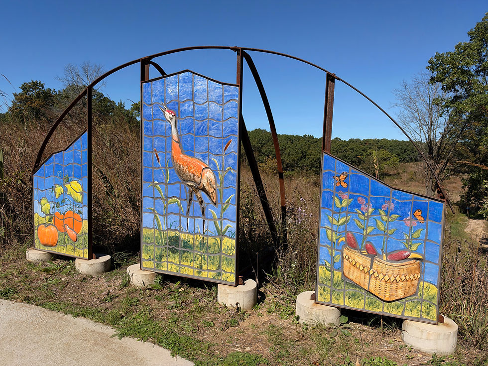 Colorful ceramic panels display nature-themed artwork, including pumpkins, a crane, and corn, set against a vibrant blue sky along a scenic path.