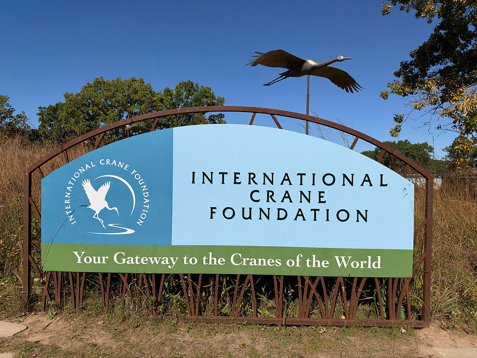 Entrance to the International Crane Foundation, surrounded by lush greenery, featuring a sign that invites visitors to discover the wonders of cranes worldwide.