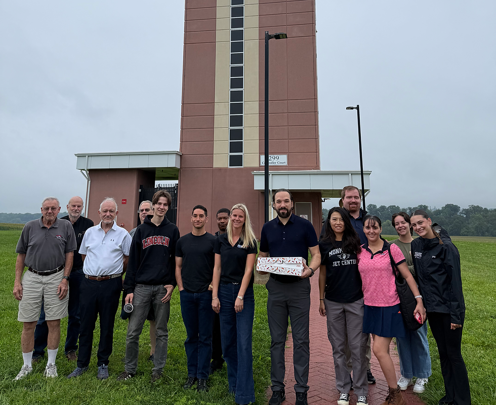 Group of Bravo Flight Training students and staff posing together outdoors in front of an airport control tower
