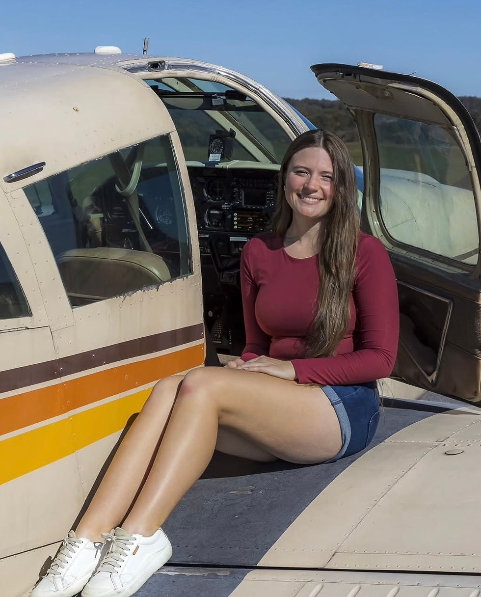 Portrait of Jovi Trimble, Administrative Assistant at Bravo Flight Training, seated in an aircraft doorway