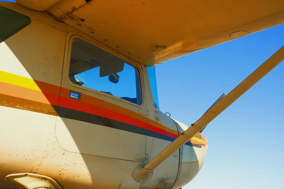Low-angle view looking up at the underside and tail of a small aircraft against a blue sky, representing the Time Building Programs