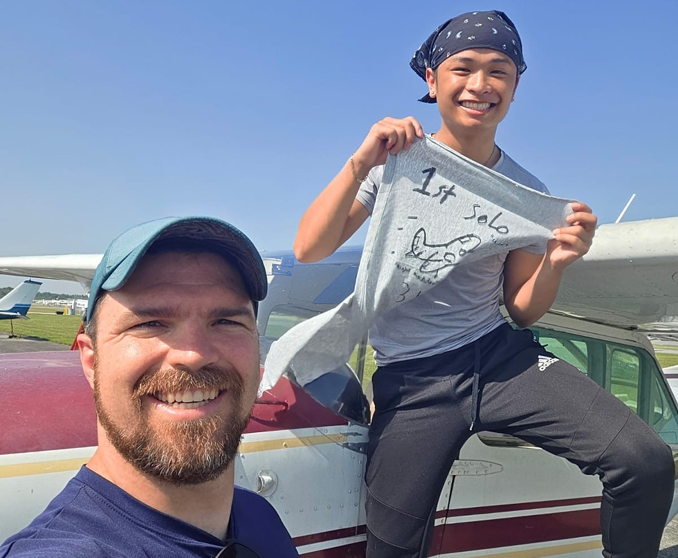 Flight instructor and student celebrating the student's first solo flight, holding a signed "1st Solo" t-shirt beside a training aircraft