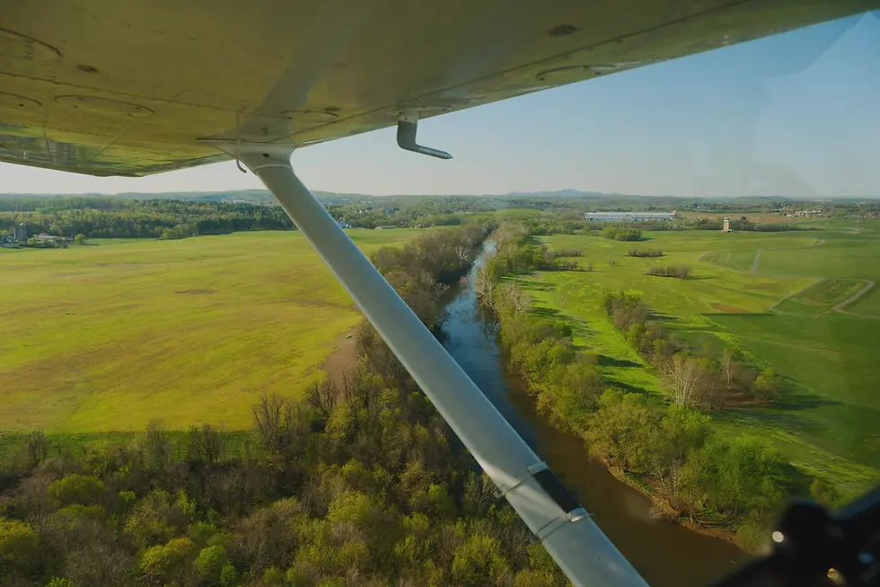 Aerial view from a small aircraft's wing looking down over green fields and a winding river, illustrating a Discovery Flight experience