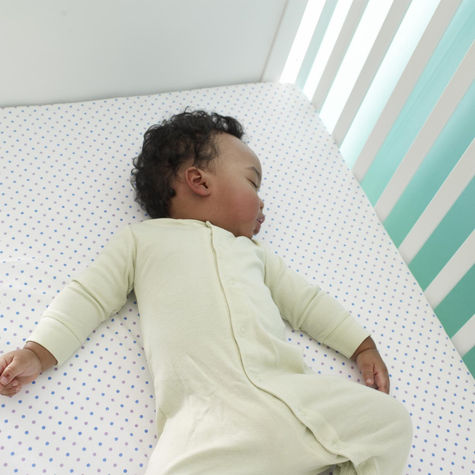 Baby peacefully sleeping on their back in a white crib with a light green onesie and polka dot crib sheet.