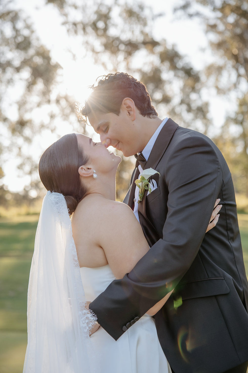 Bride and groom embracing in warm sunlight beneath garden trees