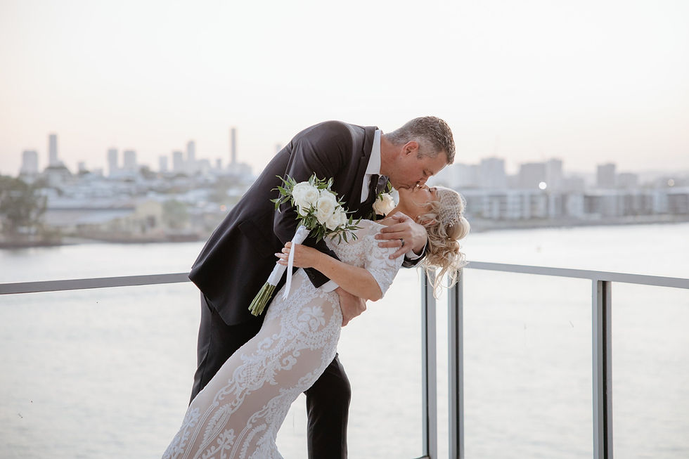 Groom dipping the bride for a kiss on a balcony overlooking a river and city skyline.