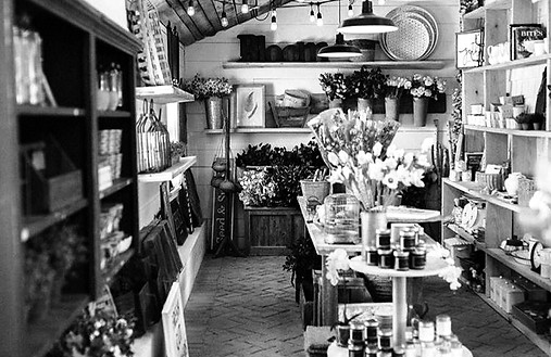 Black and white photo of shelves stocked with flowers, candles, and homewares