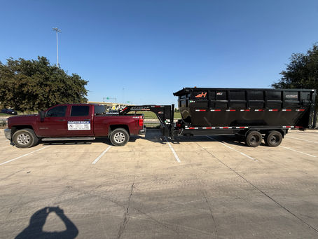 A red truck equipped with a "Dumpster Rental" sign is parked in a lot, towing a large black rolling dumpster.