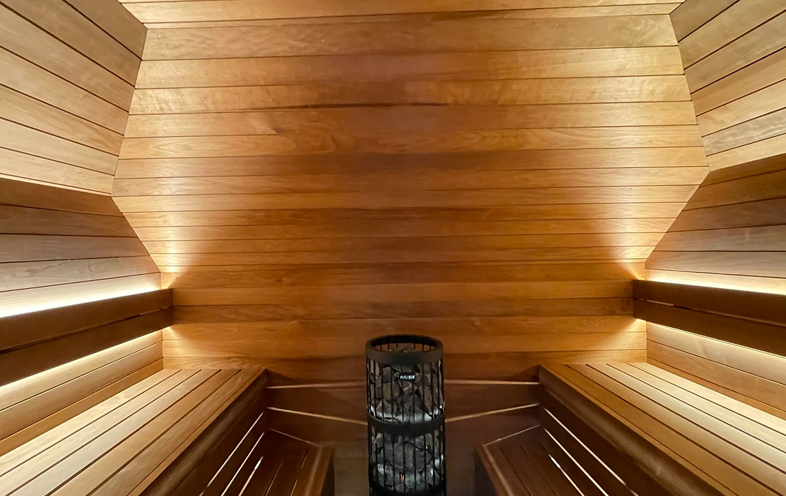 Wooden sauna interior with benches and a heater; relaxing spa experience. SAUNA COMPANY