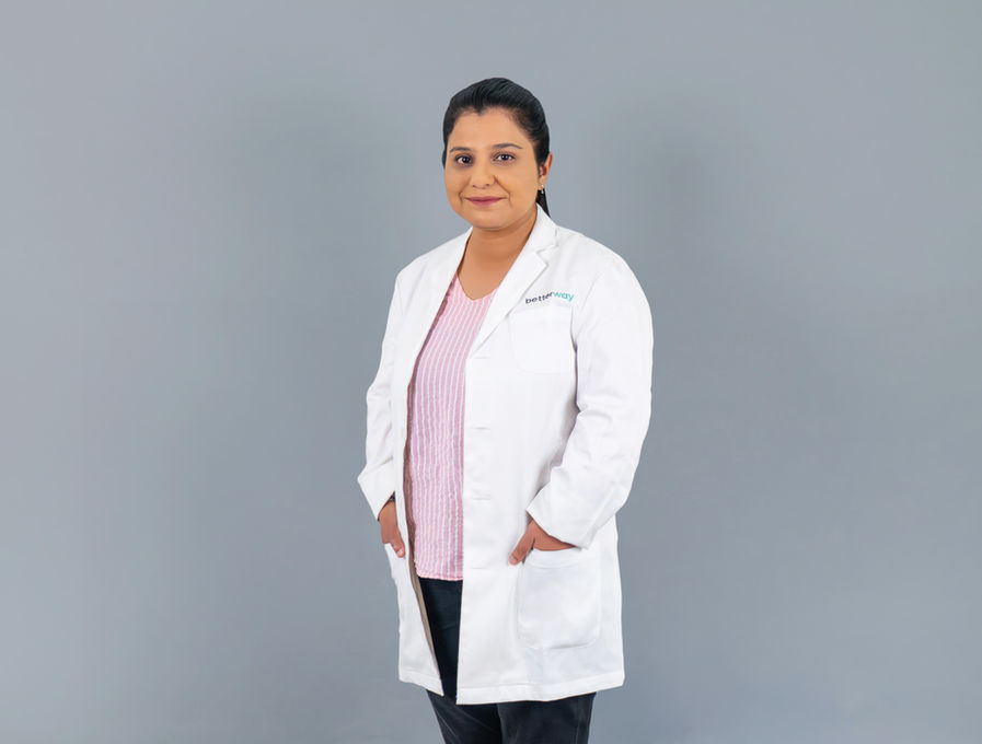 Smiling doctor in white coat stands, hands in pockets, on gray background.