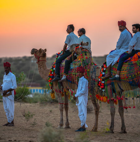 Men on camels at sunset in desert landscape. Colorful attire and hats.