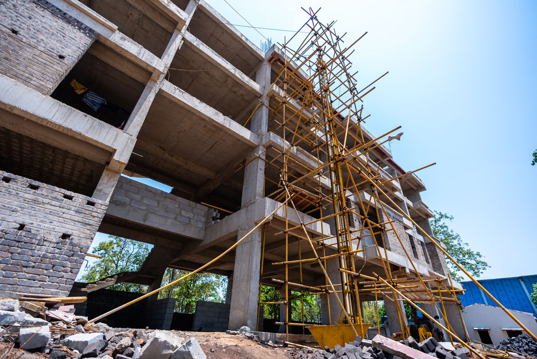 Building under construction, scaffolding supporting concrete structure, WORK PROGRESS, clear blue sky.