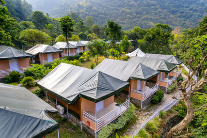 Architectural photograph of resort tents with green roofs, surrounded by lush trees and mountains in distance.