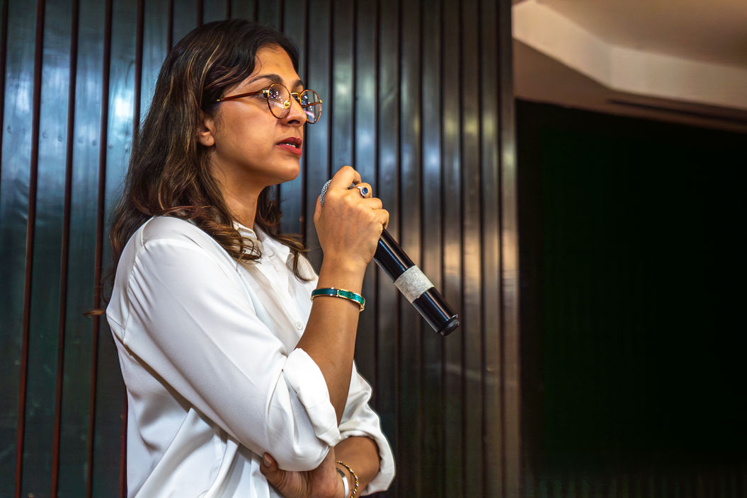 Woman with glasses holds microphone speaking at event or conference.
