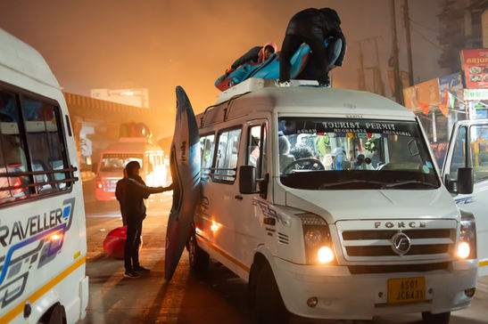 People loading surfboards onto a white tour van, TOURIST PERMIT sign visible.