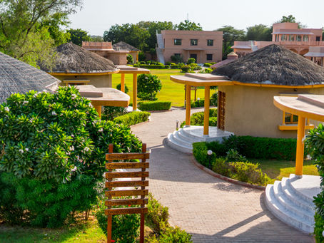 Thatched-roof cottages in a lush resort garden. Signpost with directions: Restaurant, Cottages, Swimming Pool, Spa. Bright, sunny day.